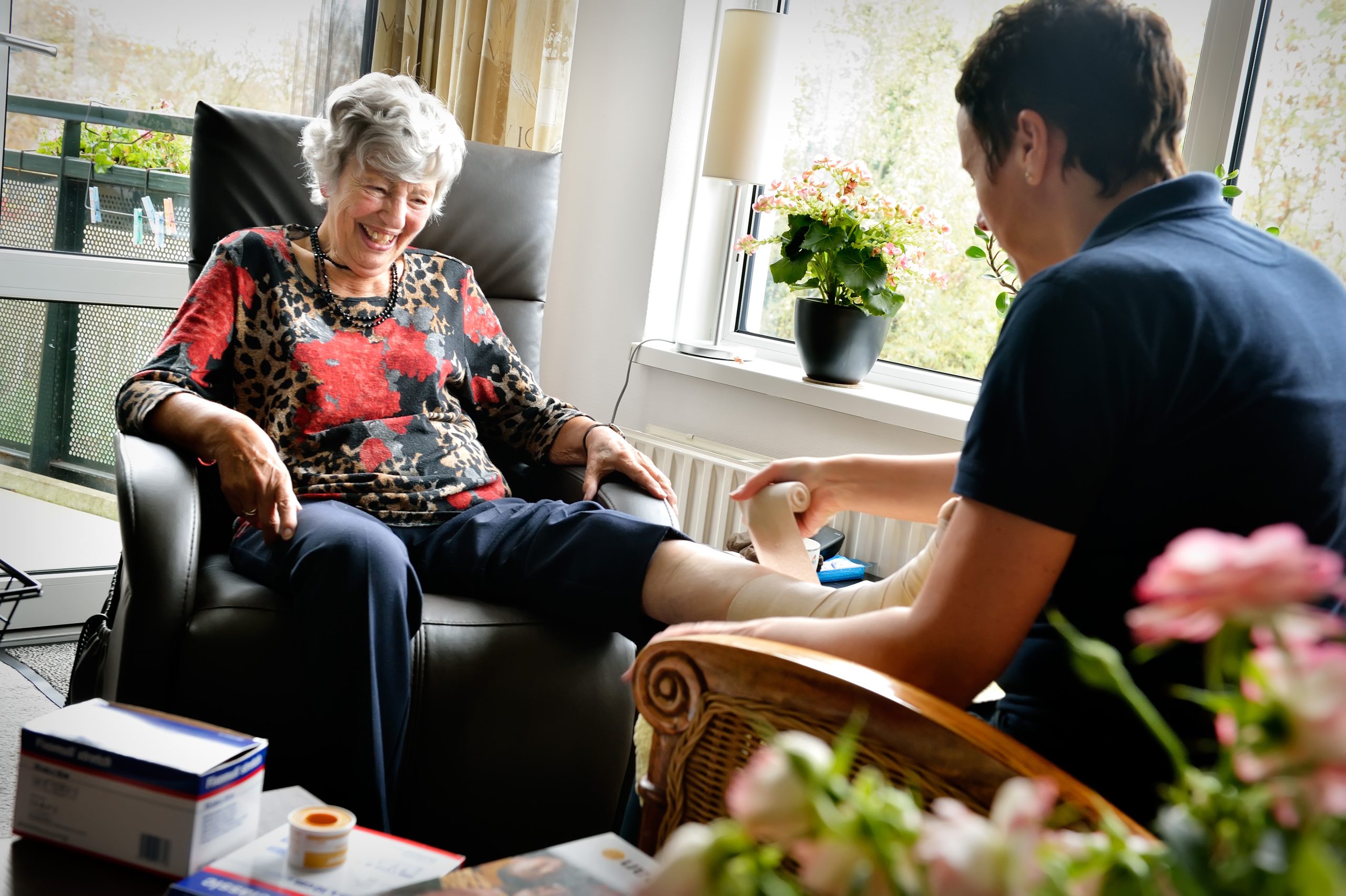 Oudere dame krijgt thuis steunkousen aan door zorgmedewerker